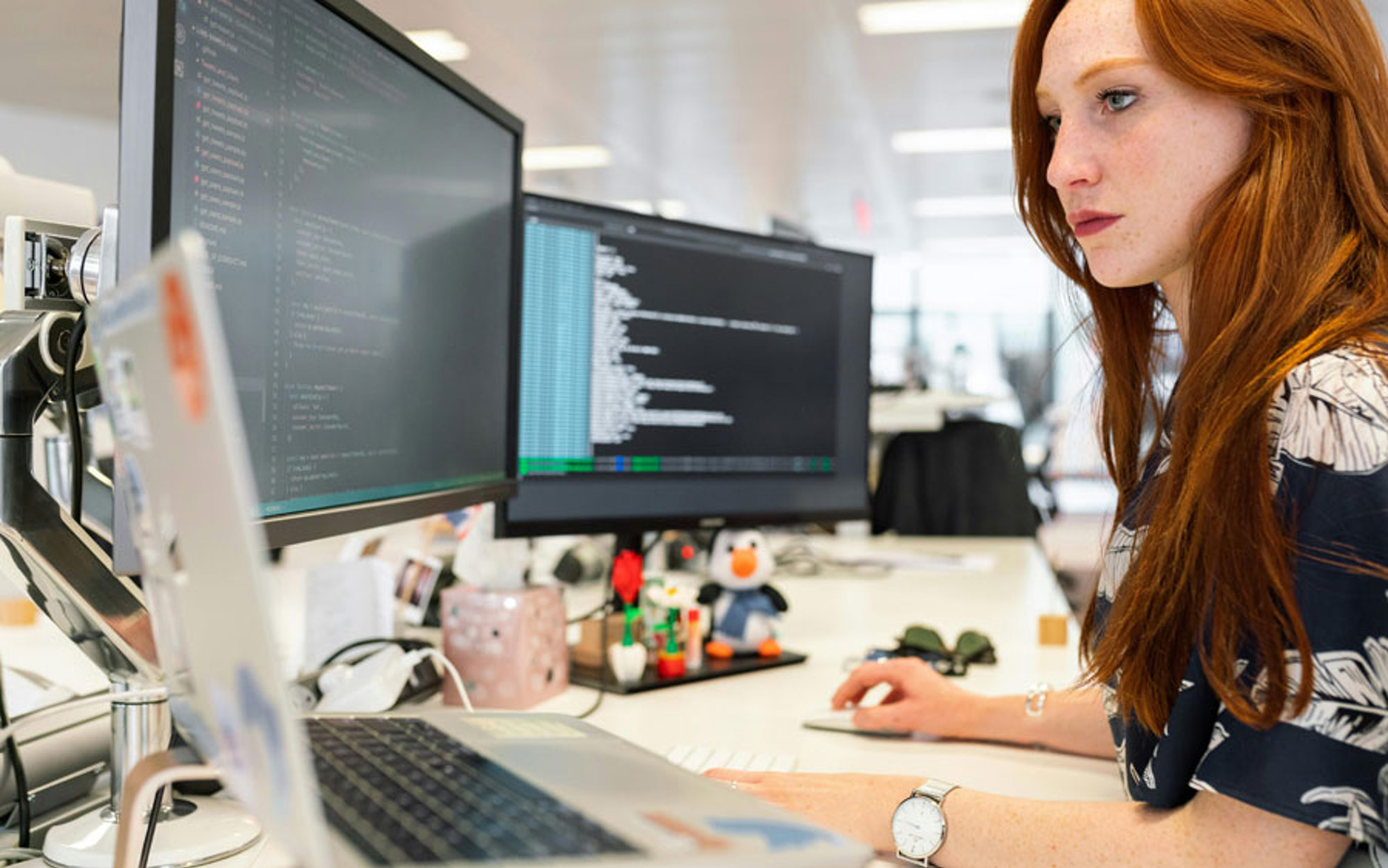 A woman working on a computer with three screens