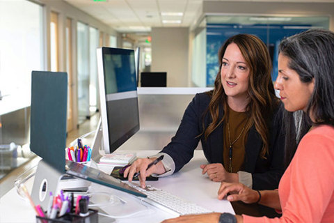 Two women working at a computer workstation