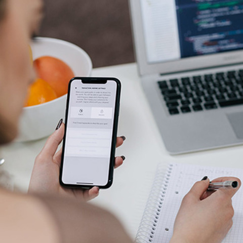 Woman browsing online on a mobile phone and taking notes
